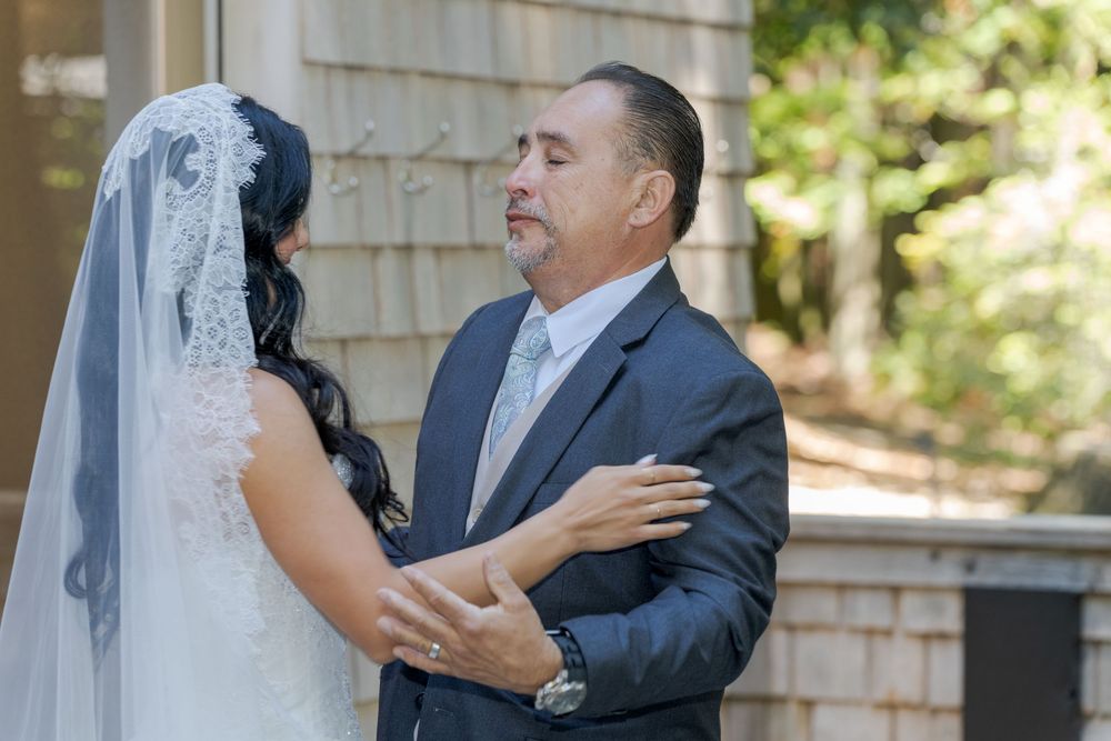 A bride in a white veil shares a tender moment with a man in a navy suit outdoors at a wedding.