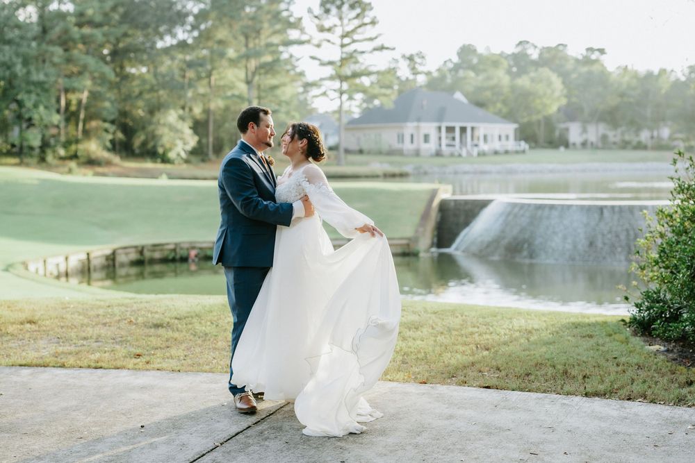Bride and groom share a romantic dance outdoors near a scenic pond and waterfall at an elegant wedding venue.
