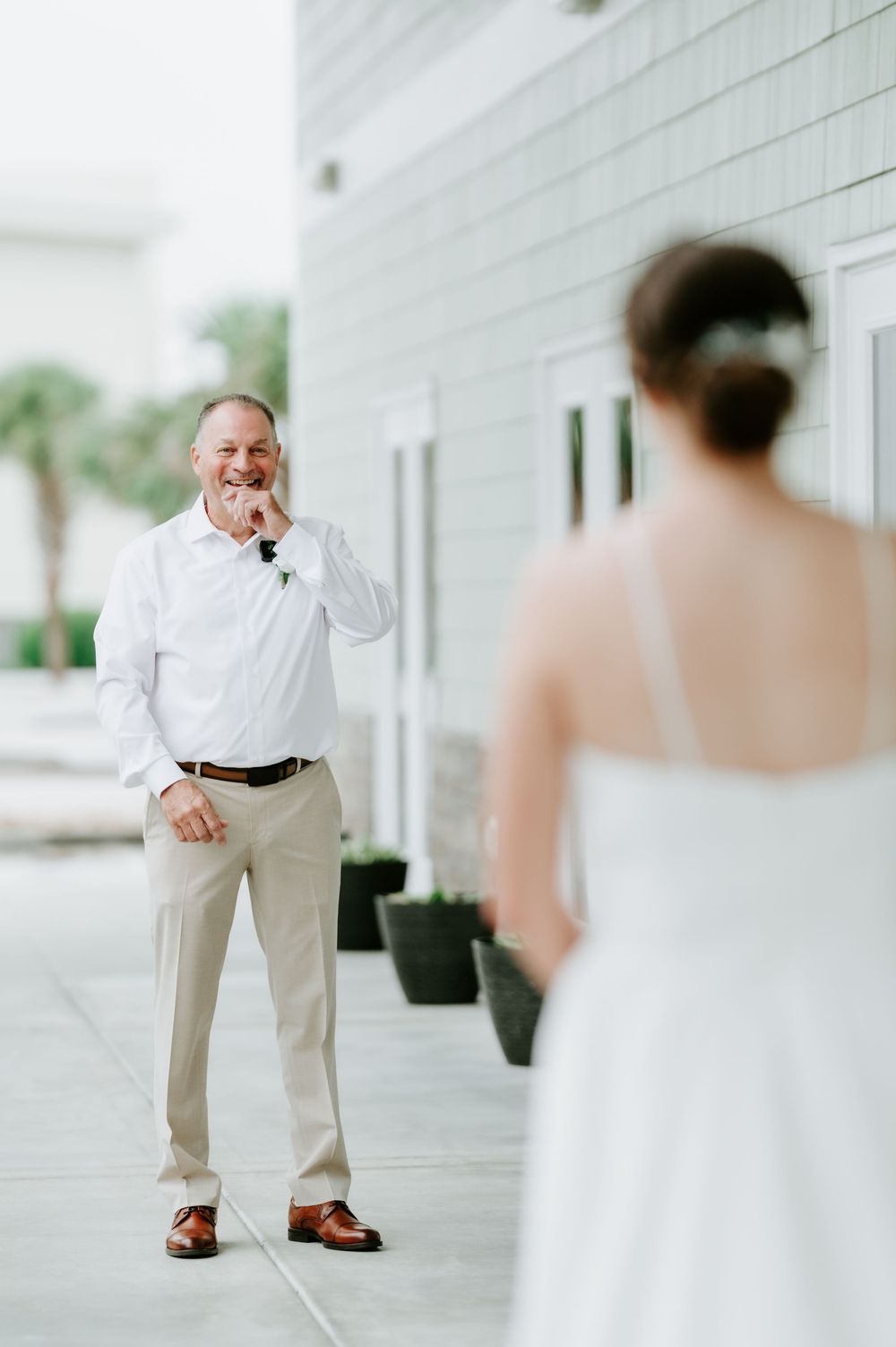 Smiling man in a white shirt and khakis covers his mouth, emotional during a wedding first look with a bride in a white gown.