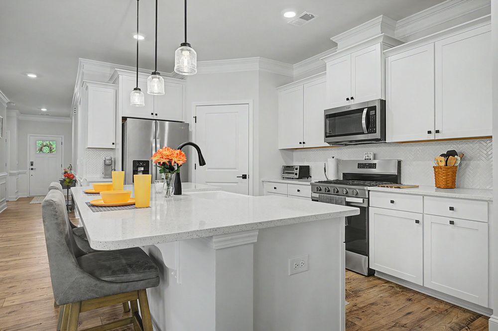 Modern white kitchen with island, quartz countertops, stainless steel appliances, pendant lights, and hardwood floors.