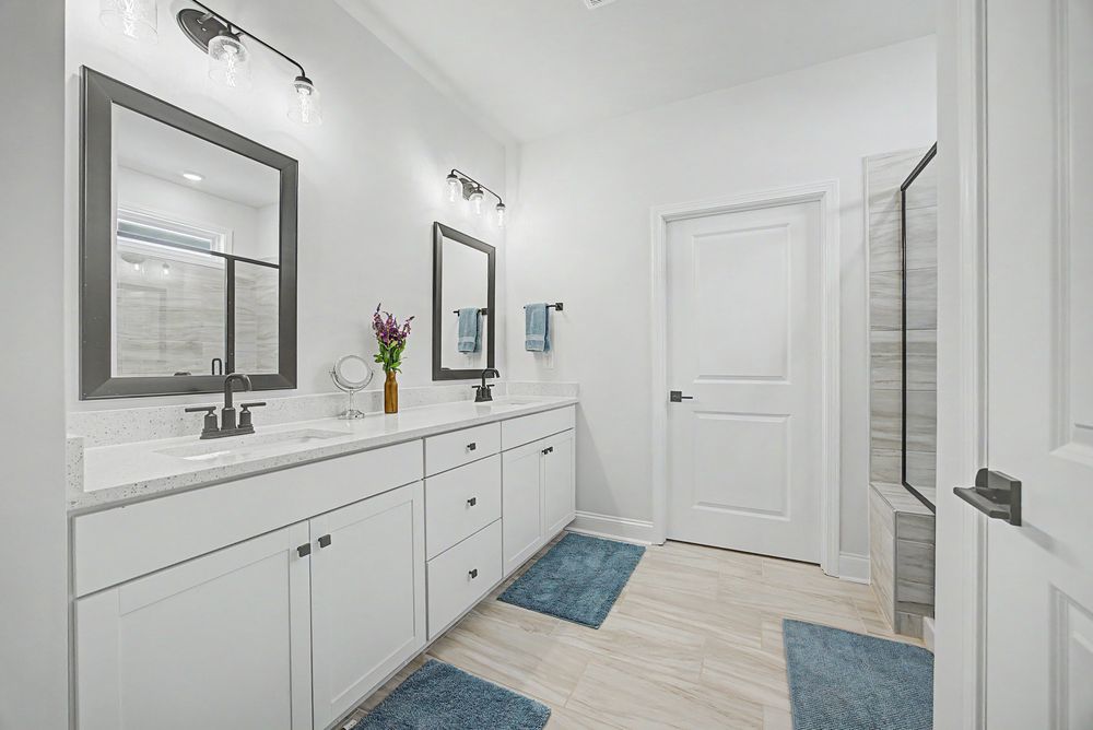 Modern bathroom with white double vanity, dual mirrors, blue rugs, and a glass shower enclosure.