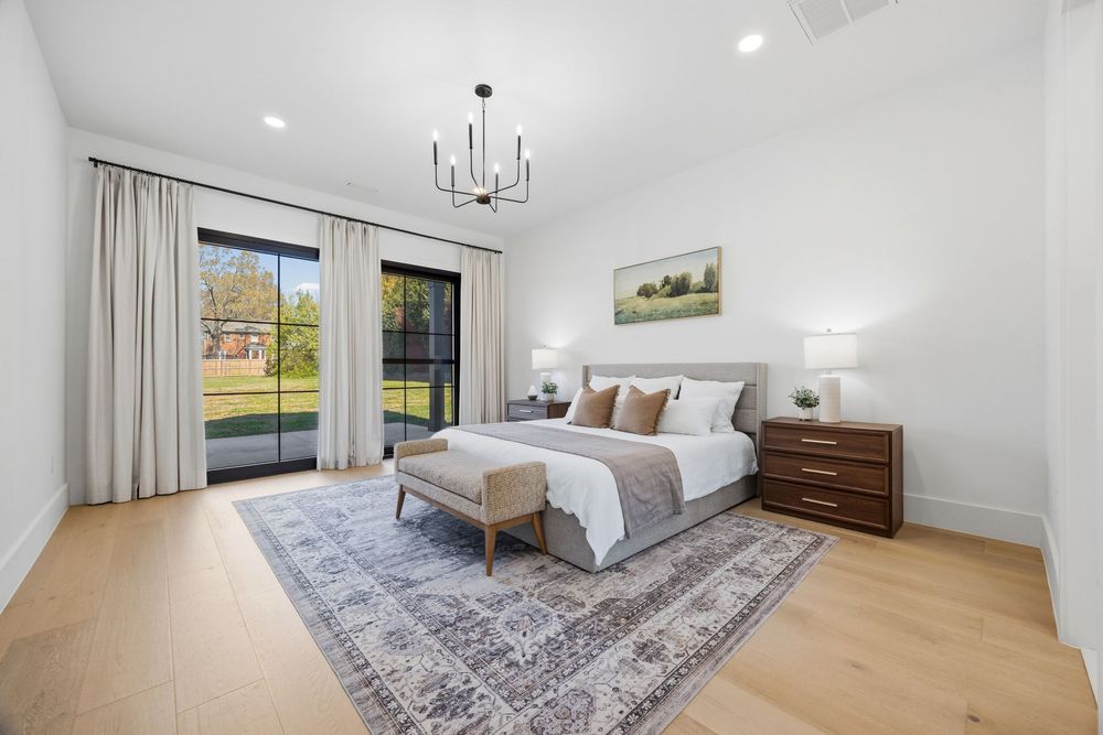 Bright master bedroom with hardwood floors, chandelier, sliding glass doors to patio, area rug, and dark wood nightstands.