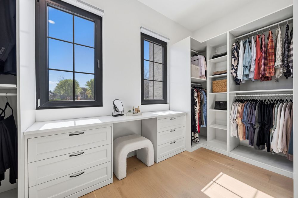 Bright walk-in closet with white built-in drawers, vanity area, open shelving, and hanging clothes rods with natural light.