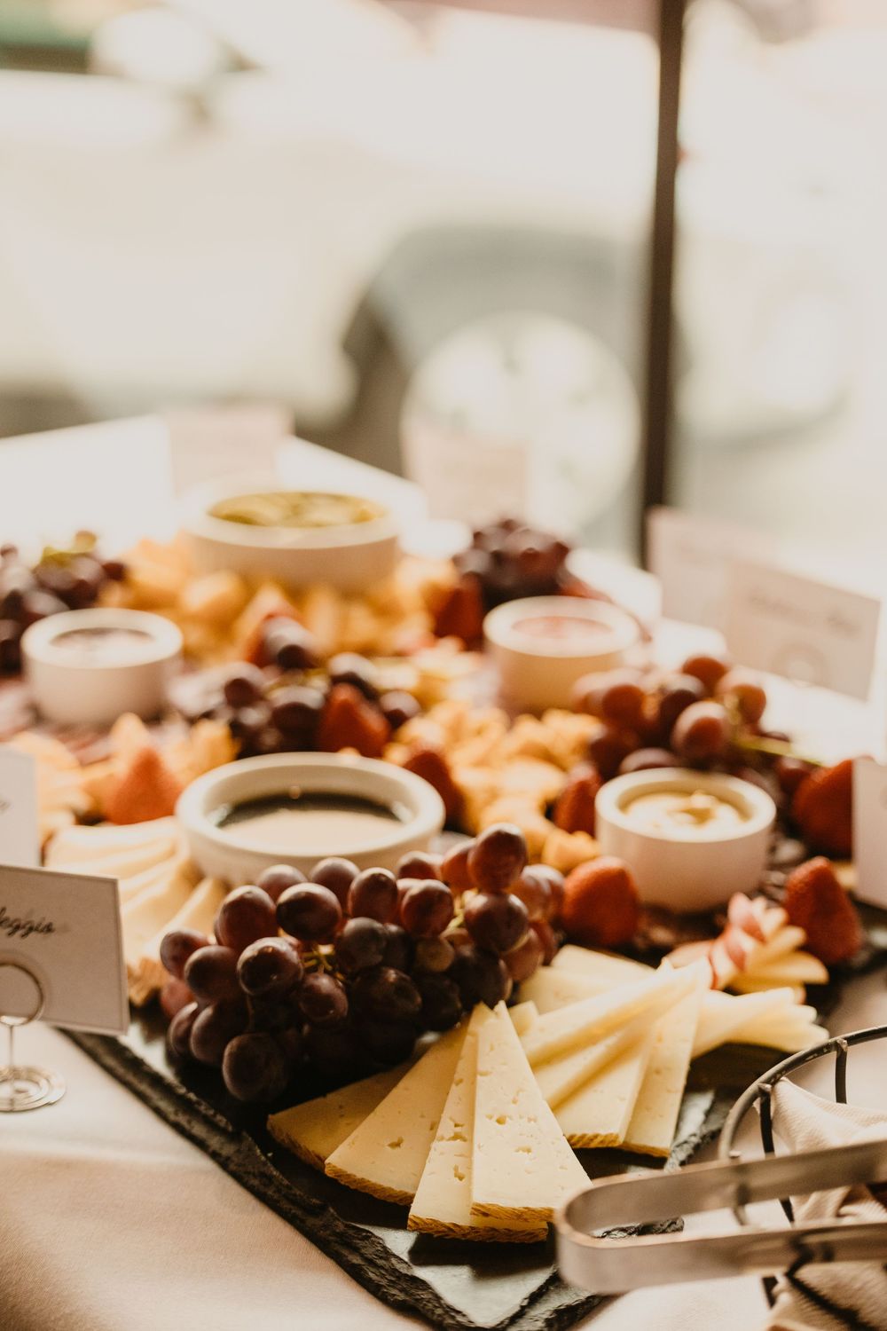 Elegant charcuterie board with cheese slices, red grapes, dipping sauces, and fresh fruits at a catered event by 2nd Street Bistro