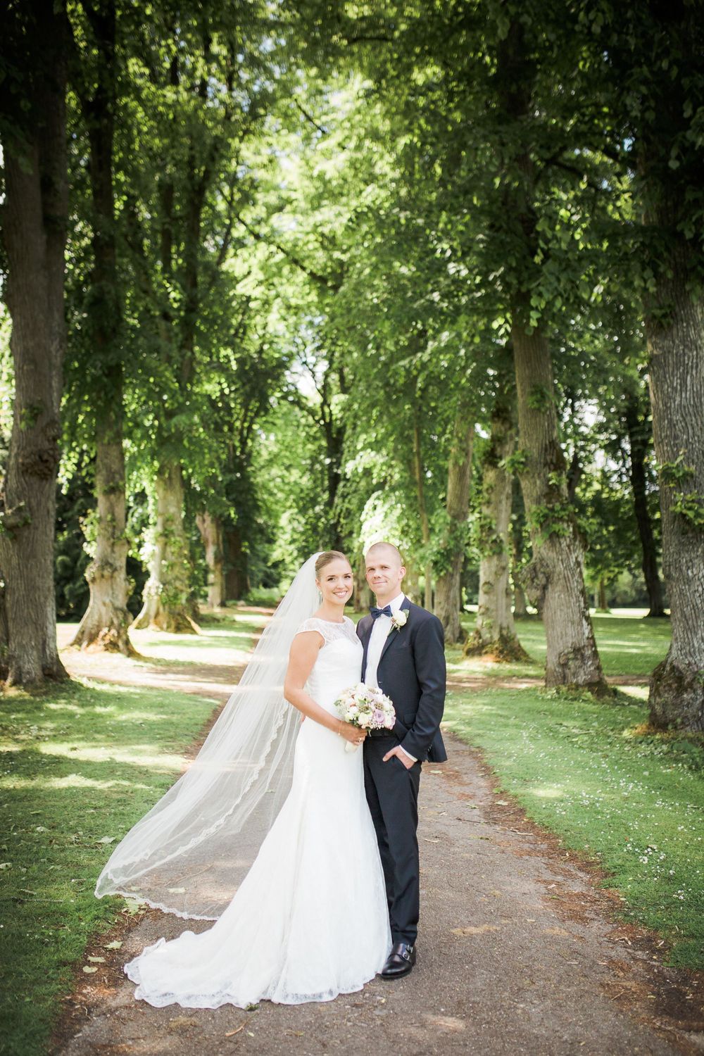 Brudepar med slør i en grøn allé – bryllupsfoto af Martin & Louise