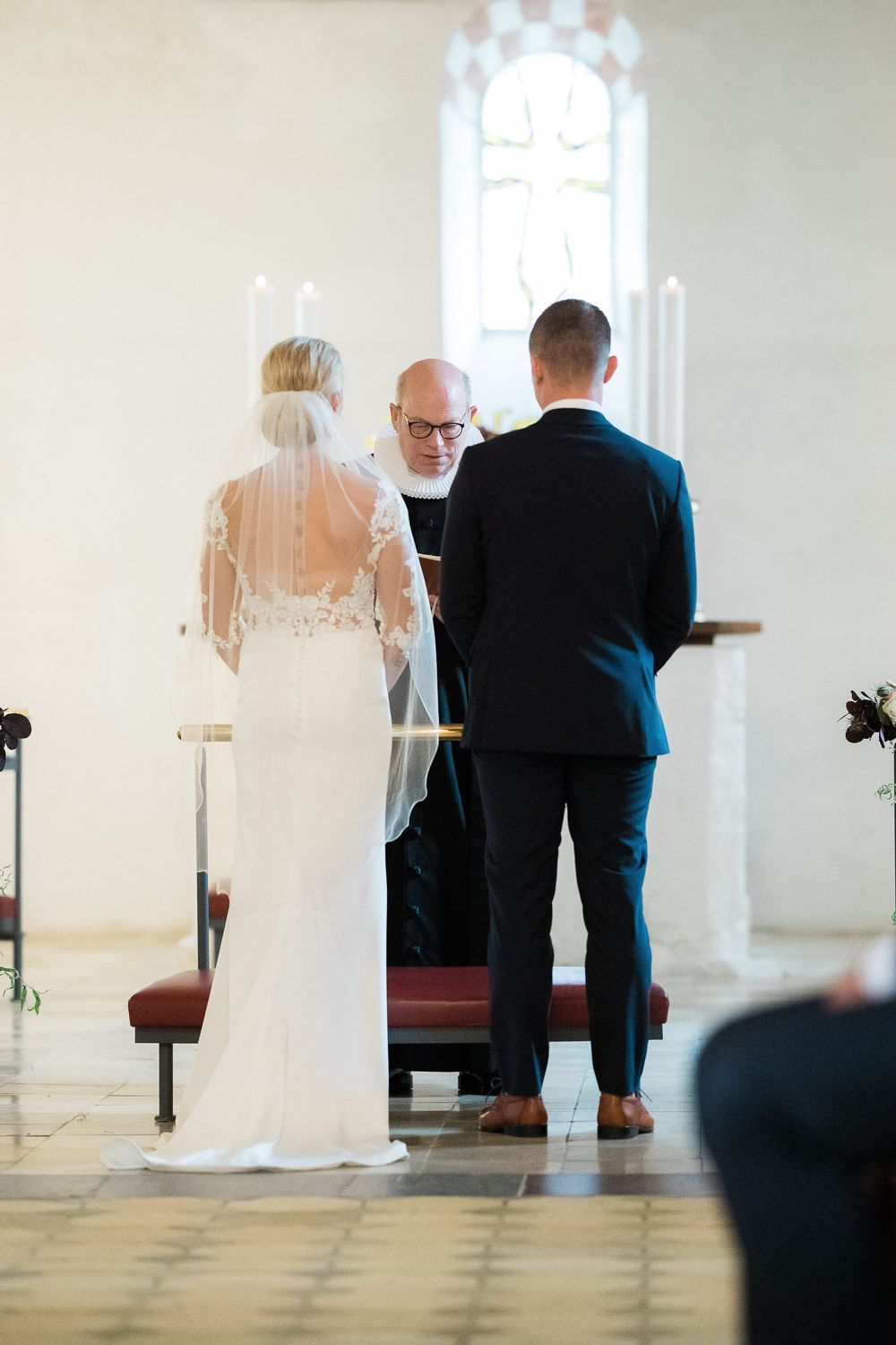 Brudepar foran præsten under kirkelig vielse – bryllupsfoto af Martin & Louise