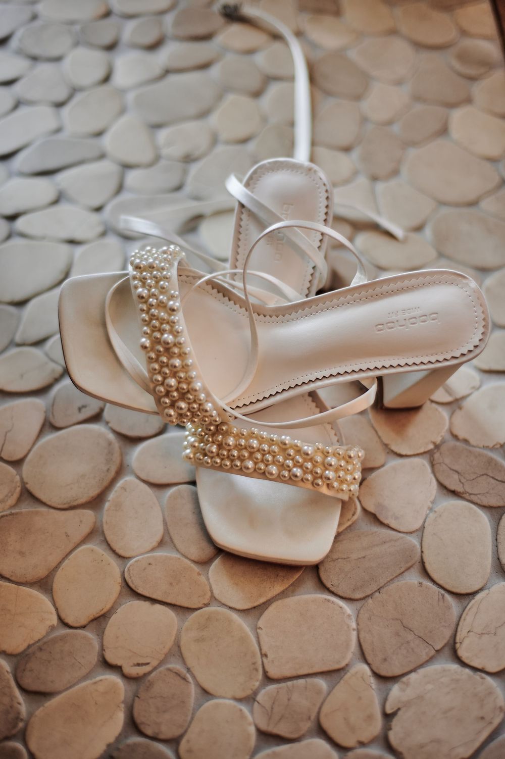 Elegant bridal heels adorned with pearl embellishments resting on a decorative stone floor.