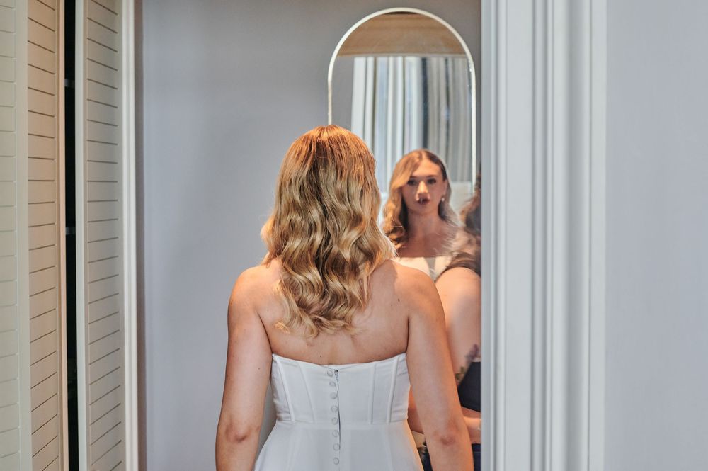 Bride in a strapless white wedding gown admiring her reflection in a full-length mirror.