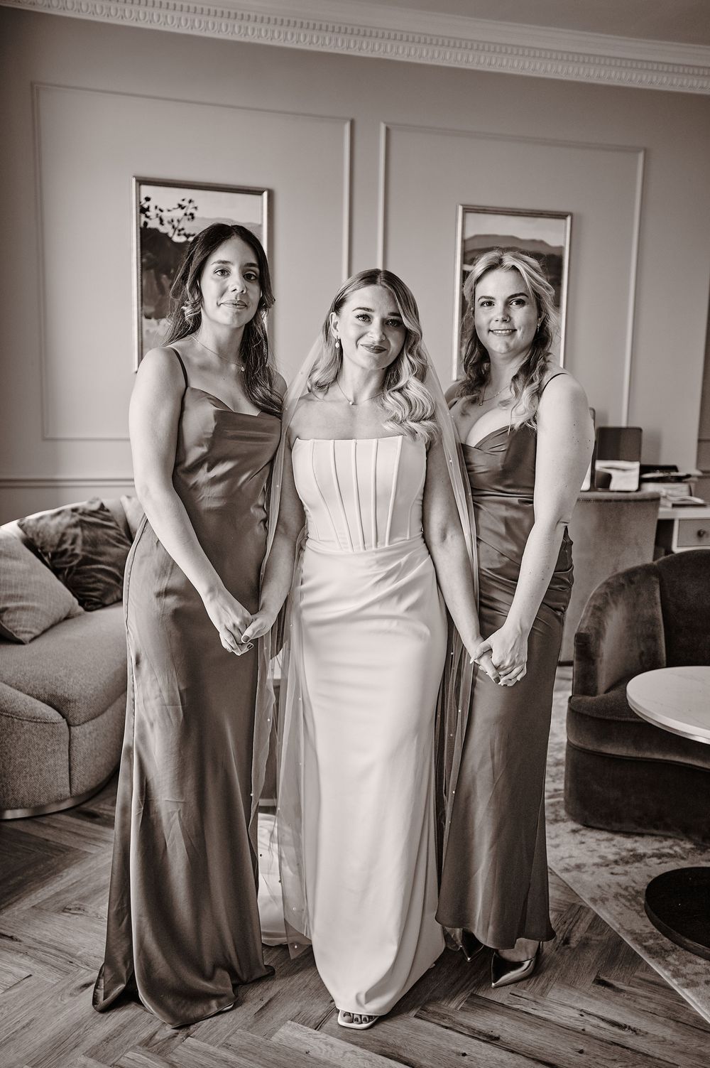 Bride in a strapless corset gown flanked by two bridesmaids in bronze satin dresses.