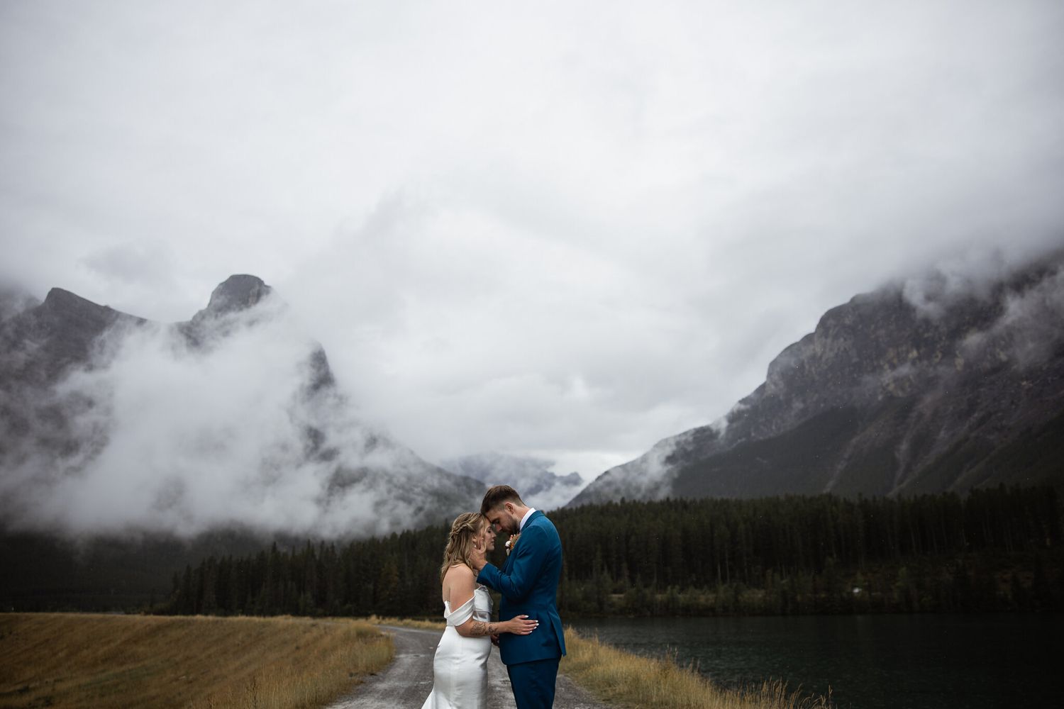 Bride and groom forehead to forehead by a mountain lake in fog, Canmore wedding photographer