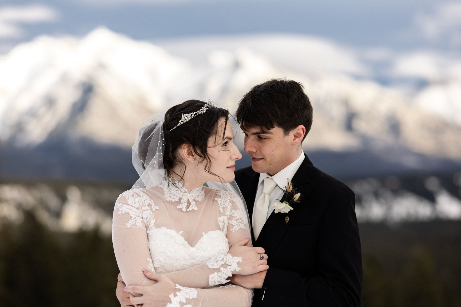 Bride and groom embracing and gazing at each other against snowy peaks at a Banff Springs winter wedding