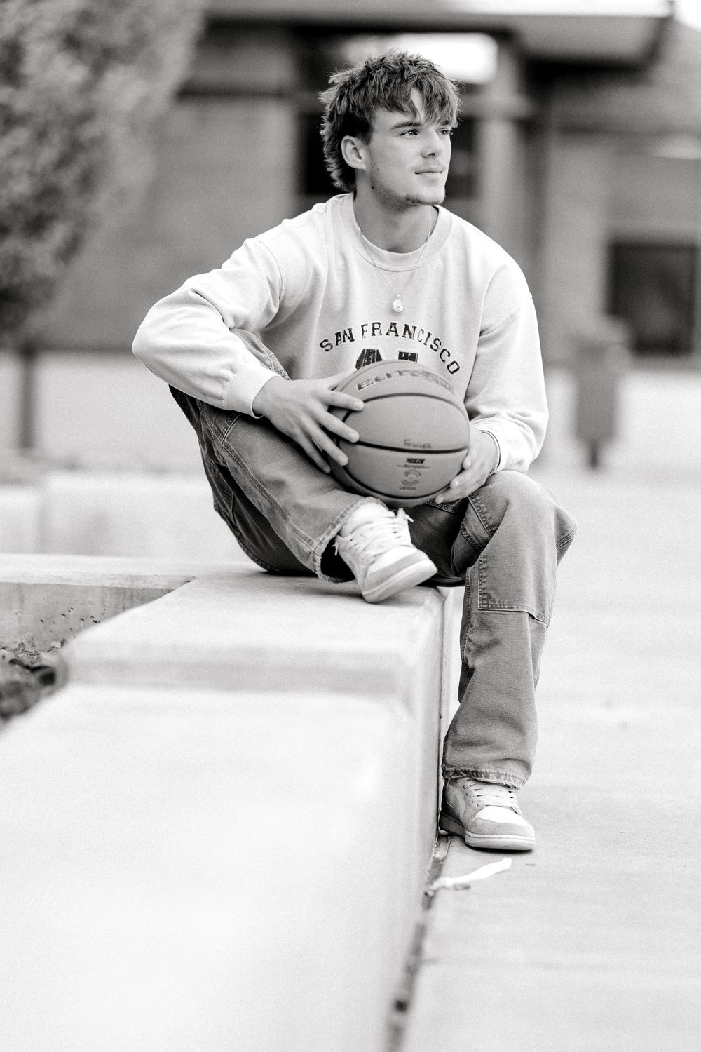 Young man in San Francisco sweatshirt sitting outdoors holding a basketball.