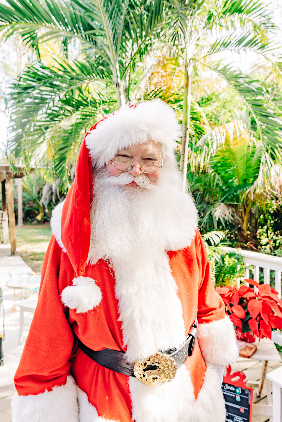Santa photos in Lake Worth Beach with Santa Claus surrounded by tropical greenery and Christmas poinsettias.