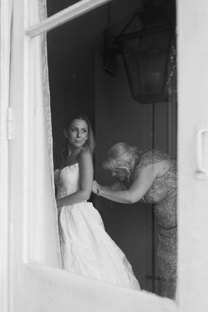 Black and white photo of mother fastening bride's wedding gown in a doorway.