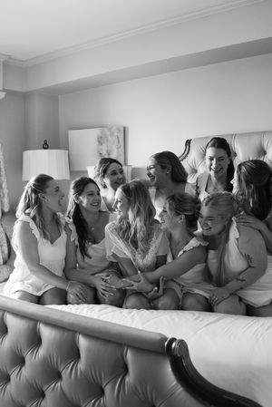 Black and white photo of bridesmaids laughing together on a tufted bed before the wedding.