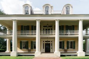Grand Southern plantation home with yellow facade, white columns, and wraparound porch.