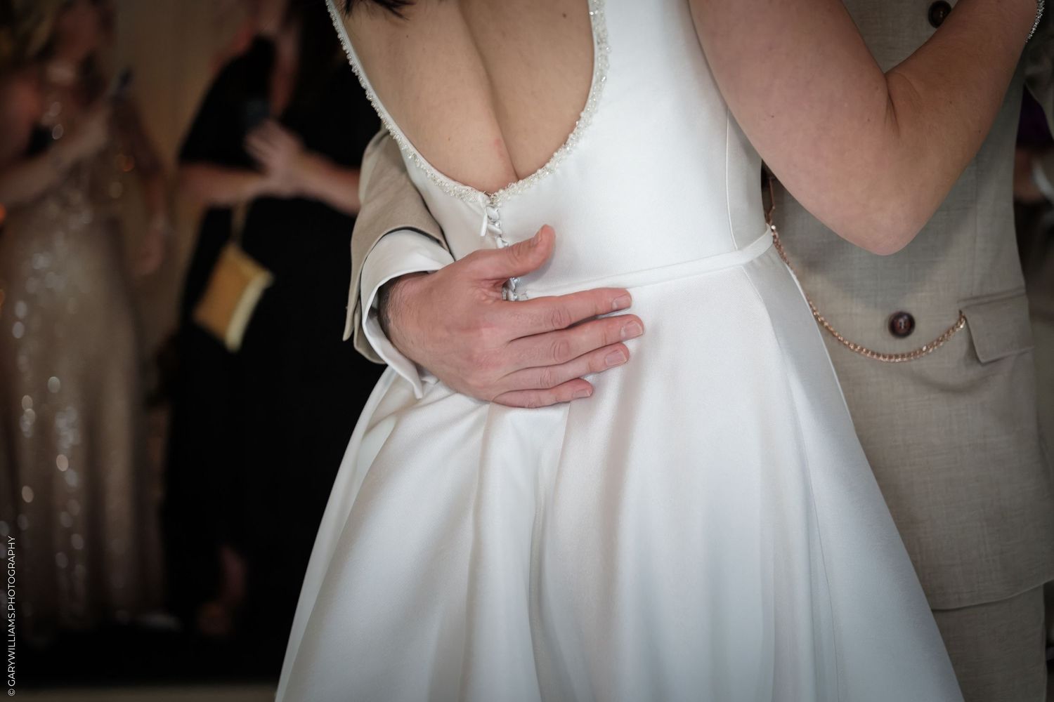 Groom embracing bride in elegant white wedding dress with deep V-back neckline during romantic first dance.