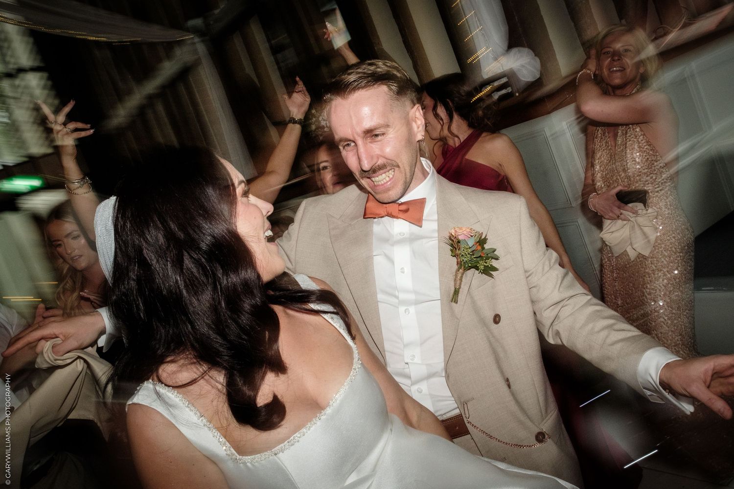 Bride and groom share a joyful dance together at their wedding reception surrounded by celebrating guests.