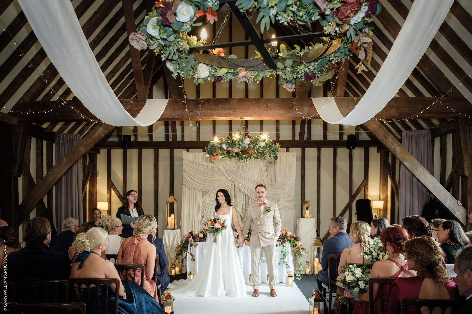 Couple exchanges vows in a rustic barn wedding venue adorned with floral arrangements and white draping.