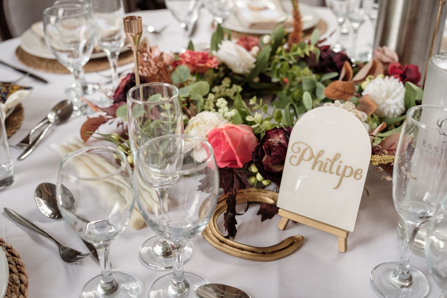 Elegant wedding table setting with floral centerpiece, crystal glassware, and a gold name card reading Philipe.