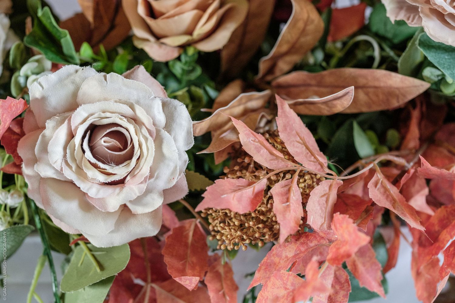 Autumn floral arrangement featuring cream roses, russet brown leaves, and red foliage with green berry accents.