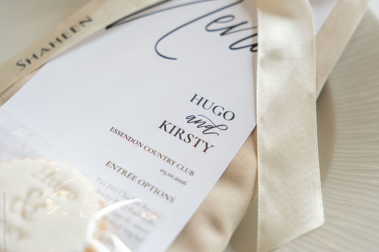 Elegant wedding menu card for Hugo and Kirsty at Essendon Country Club, tied with a cream satin ribbon.