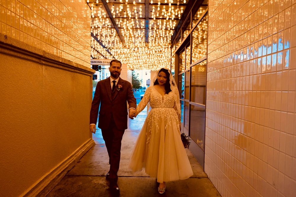 Bride and groom walk hand in hand through a tiled alley glowing with string lights at a Las Vegas wedding.