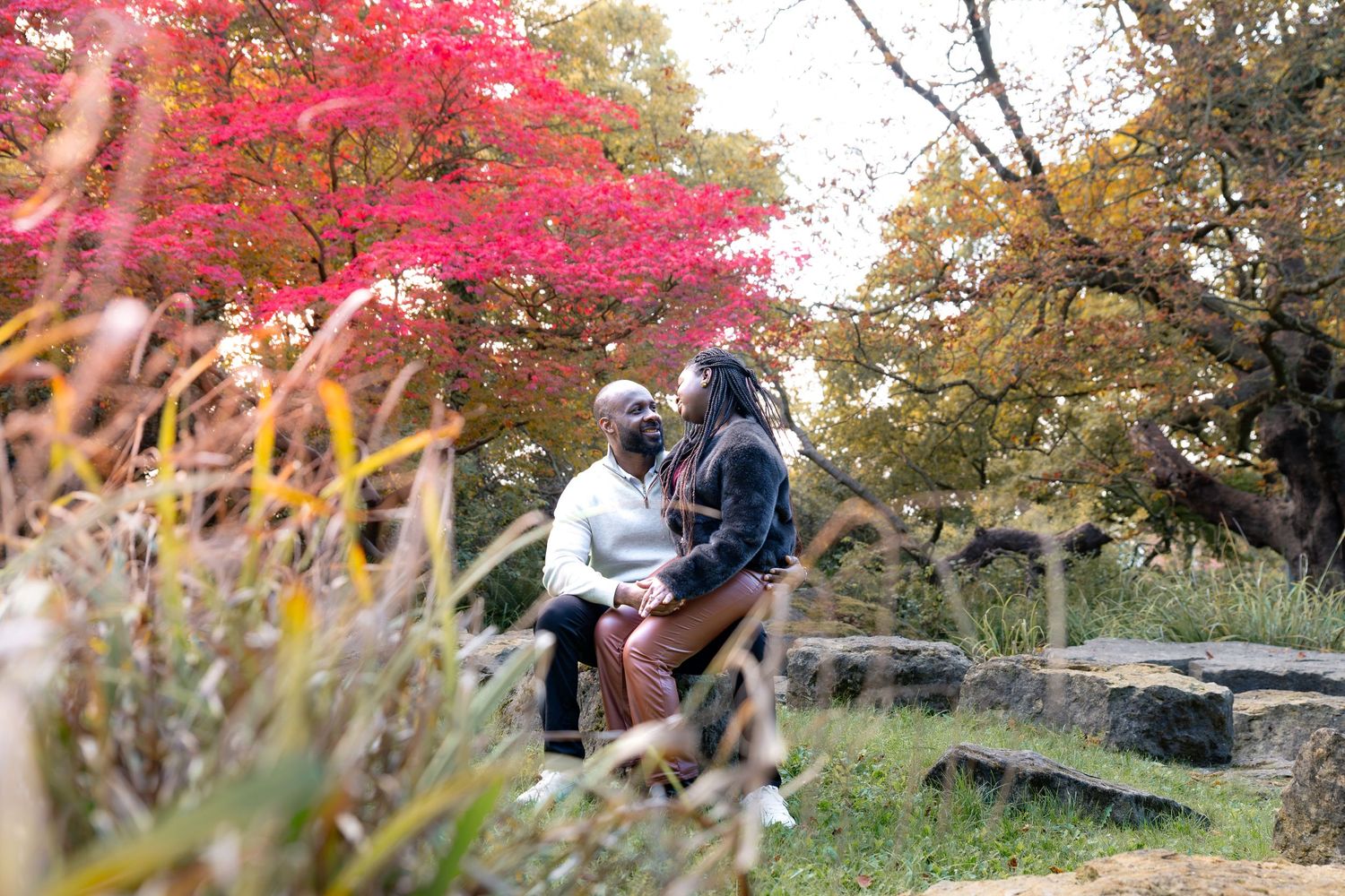 Couple embracing outdoors in autumn park with vibrant red Japanese maple tree and colorful fall foliage. Engagement photography Rotherham