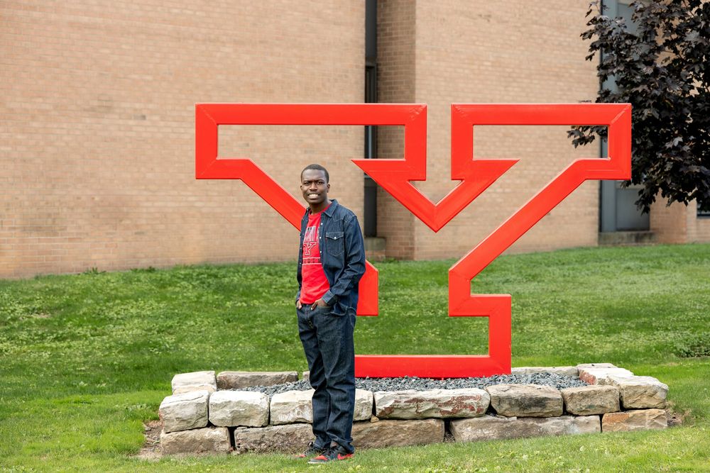Young Black man standing in front of a large red Youngstown State University Y logo sculpture on campus.