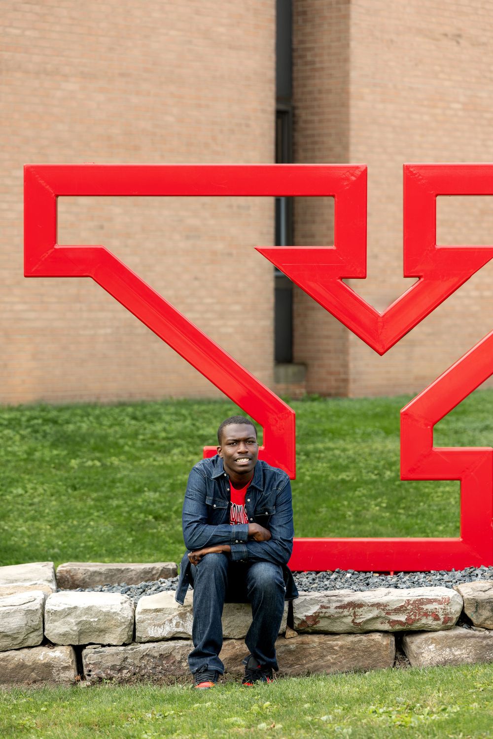Young Black man sitting in front of large red Y sculpture on college campus lawn.
