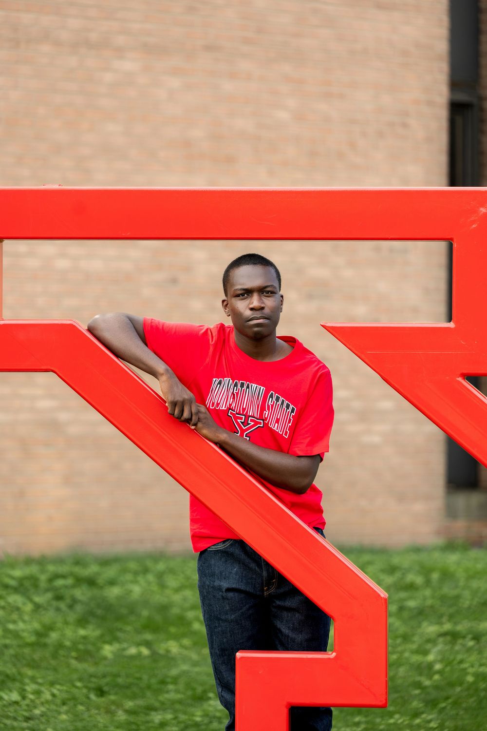 Young Black man in red Youngstown State shirt leaning on large red Y sign.