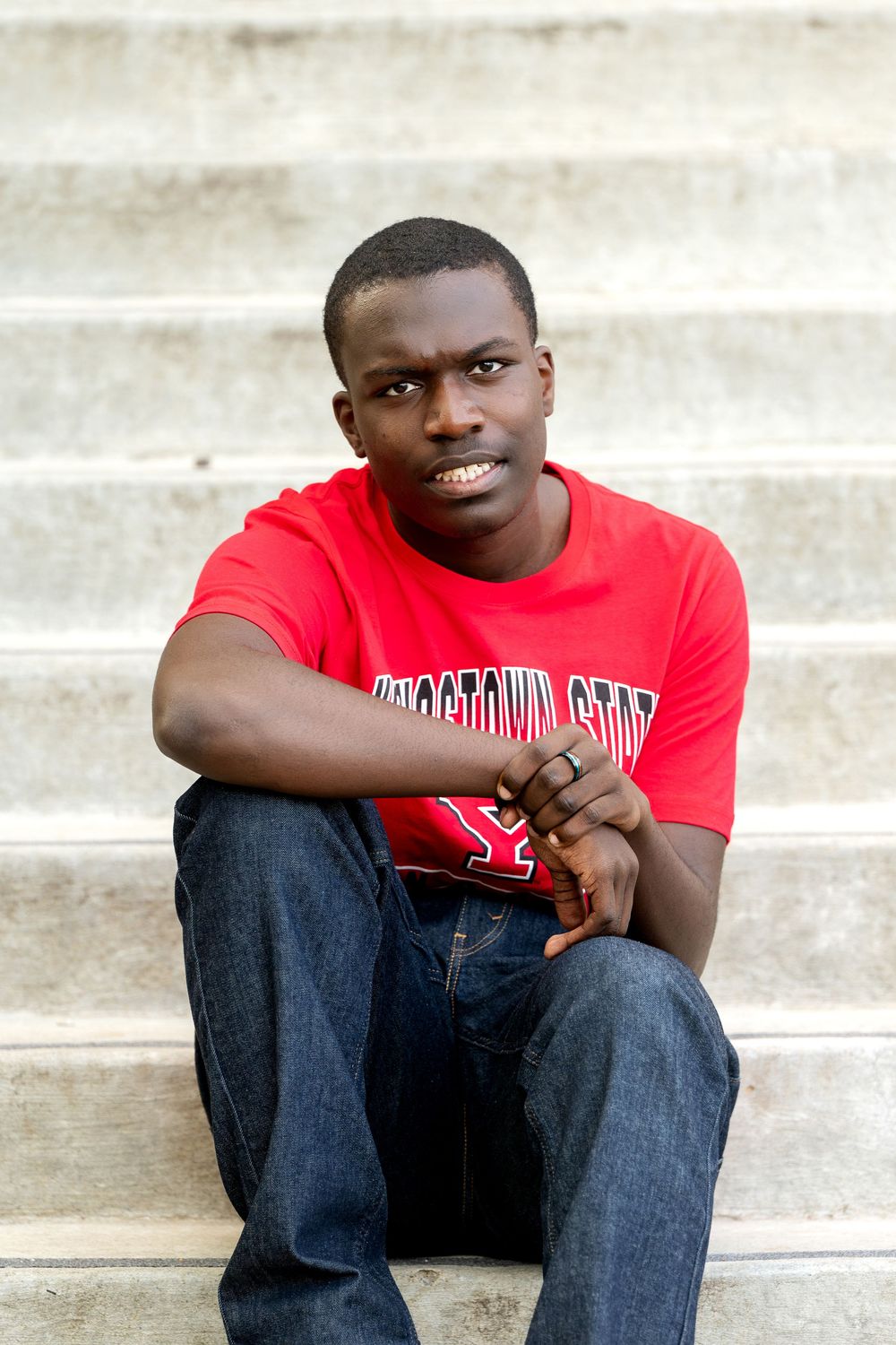 Young Black man in red Youngstown State shirt sitting on concrete steps outdoors.