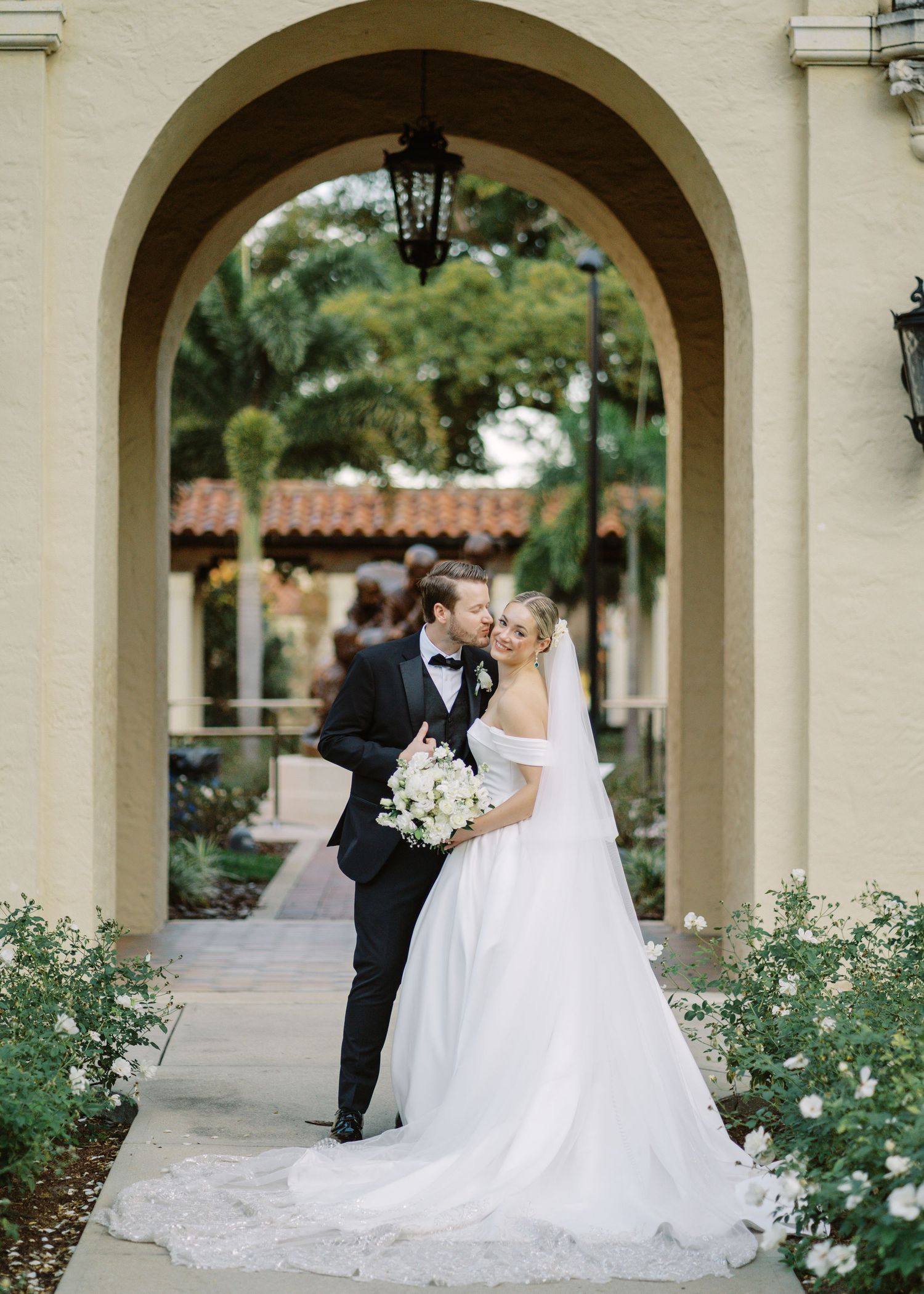 Bride and groom share a romantic kiss under an elegant arched doorway at a Mediterranean-style wedding venue.