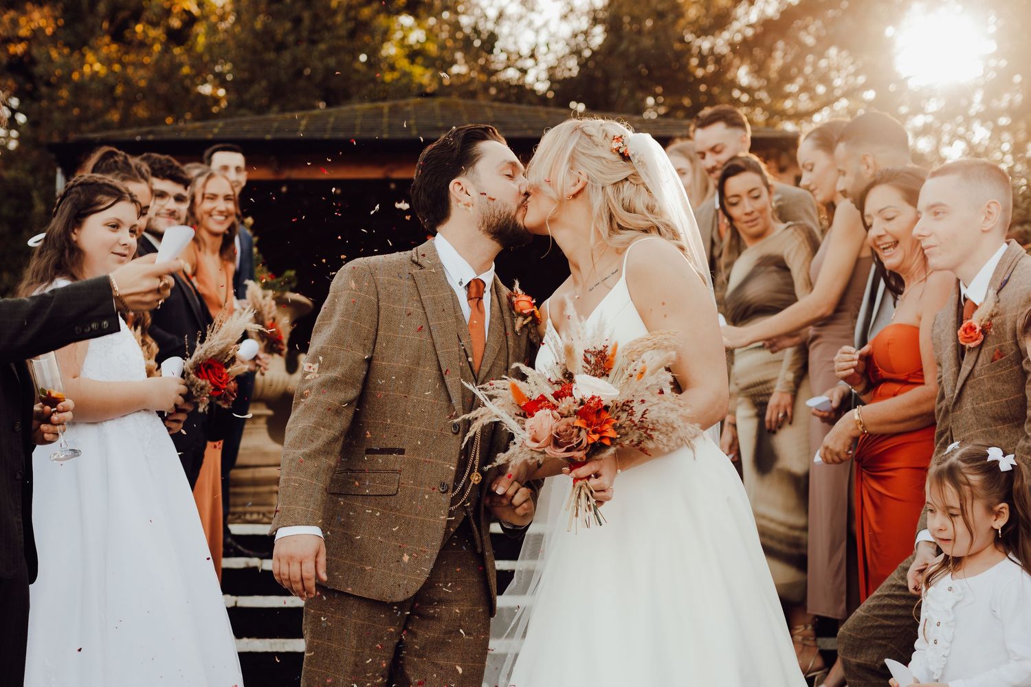 The October wedding couple celebrating with guests during a confetti toss outdoors.
