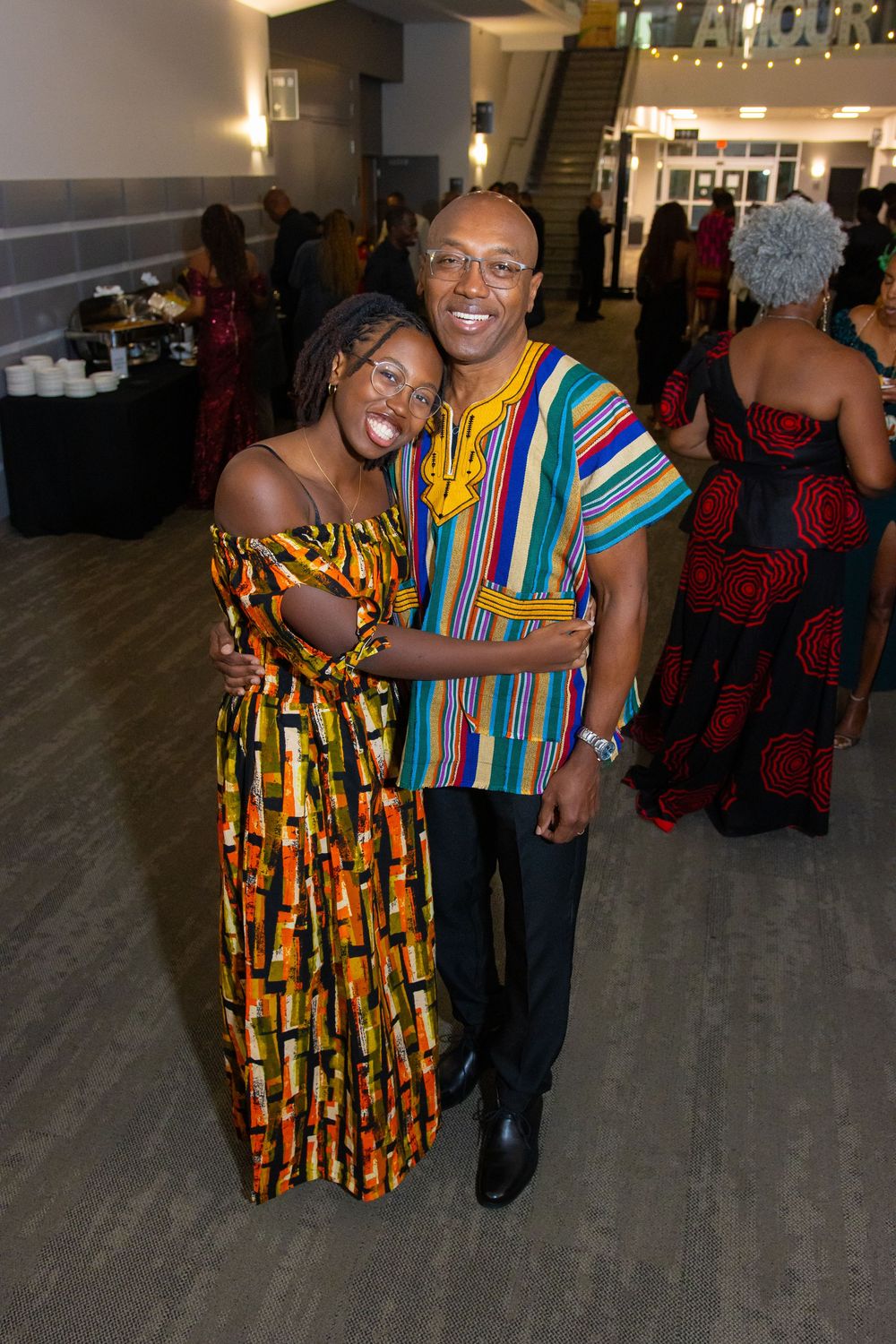 Two people in vibrant African print attire smile and pose together at a formal evening event.
