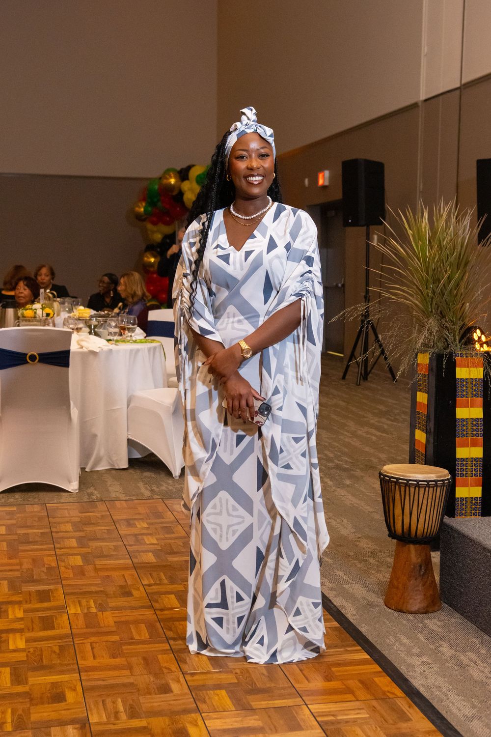 Woman wearing blue geometric African kaftan and matching headwrap at formal cultural event.
