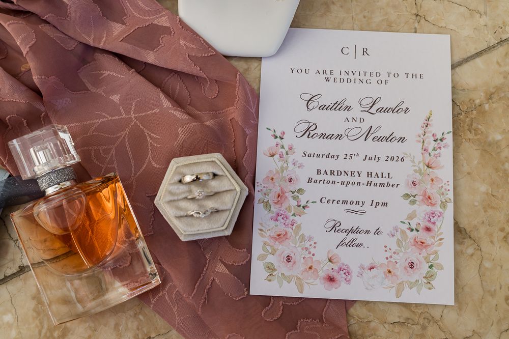 Wedding invitation for Caitlin Lawler and Ronan Norton at Bardney Hall, displayed with rings and perfume bottle.