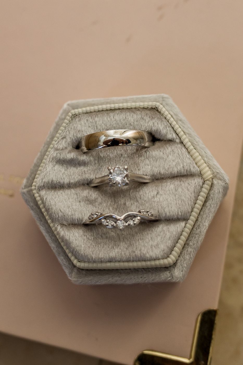 Three silver rings in a gray hexagonal velvet ring box, including a solitaire diamond engagement ring and two wedding bands.