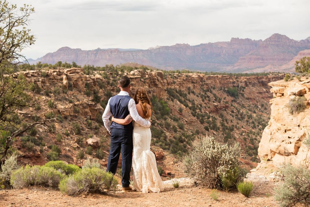 Bride and groom embrace overlooking stunning Zion National Park canyon landscape on their wedding day.