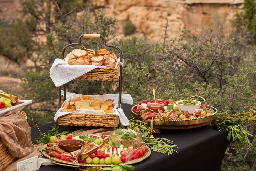 Outdoor charcuterie spread with bread, grapes, strawberries, and meats on a black table with desert scenery.