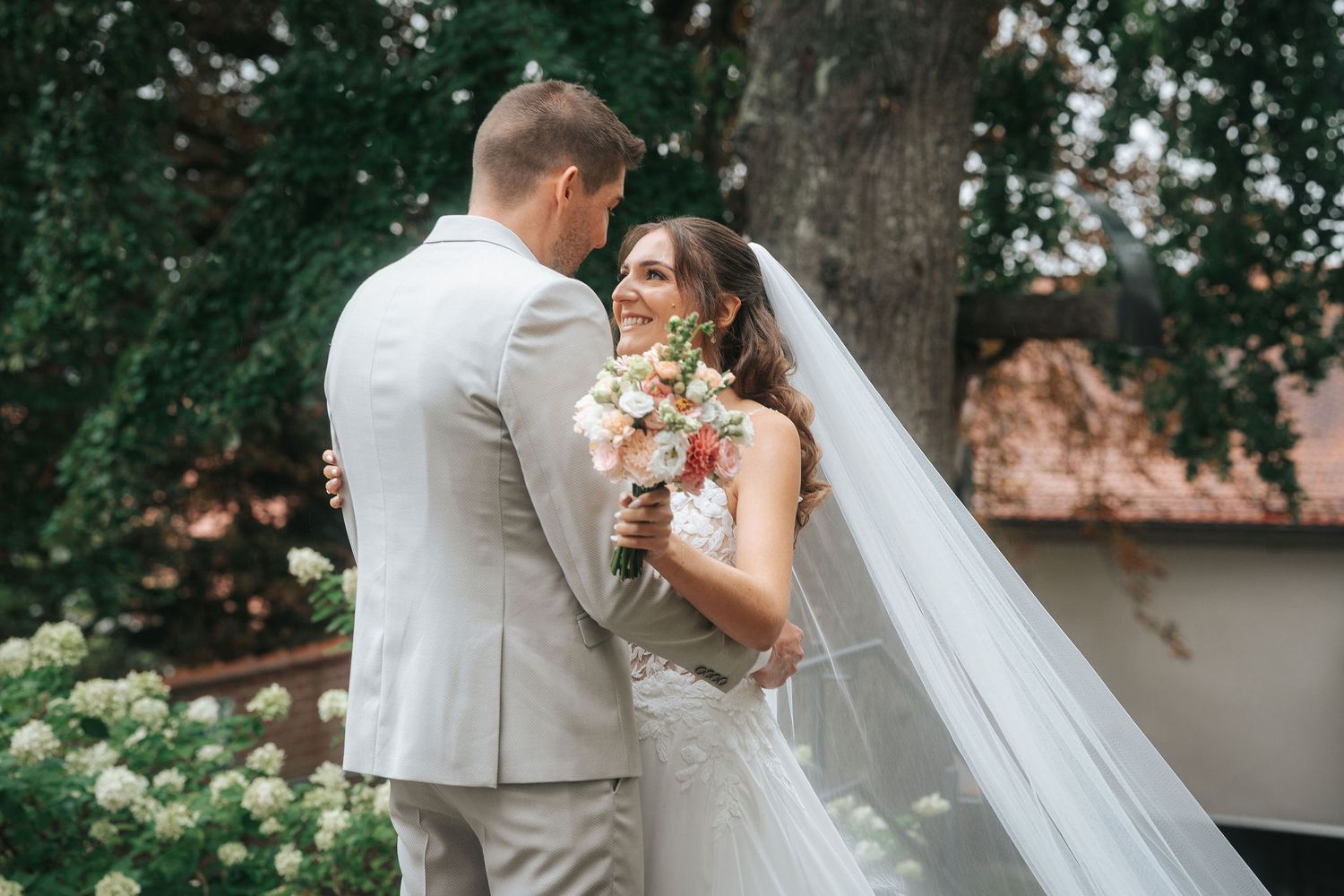A couple in wedding attire stands together during golden hour in a scenic outdoor setting.