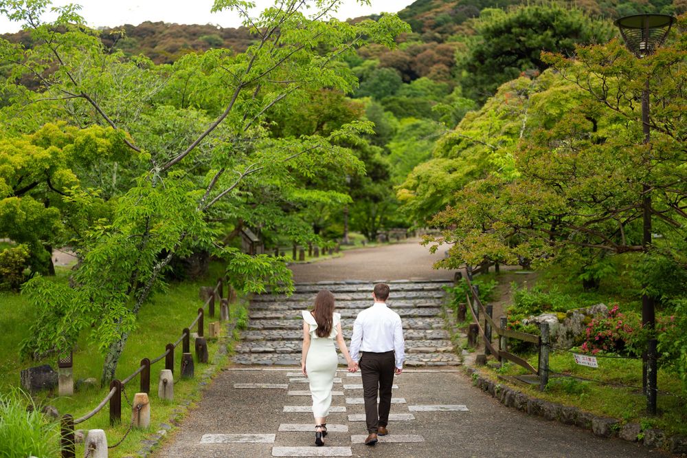 Couple walking hand in hand up stone steps through a lush green Japanese garden.