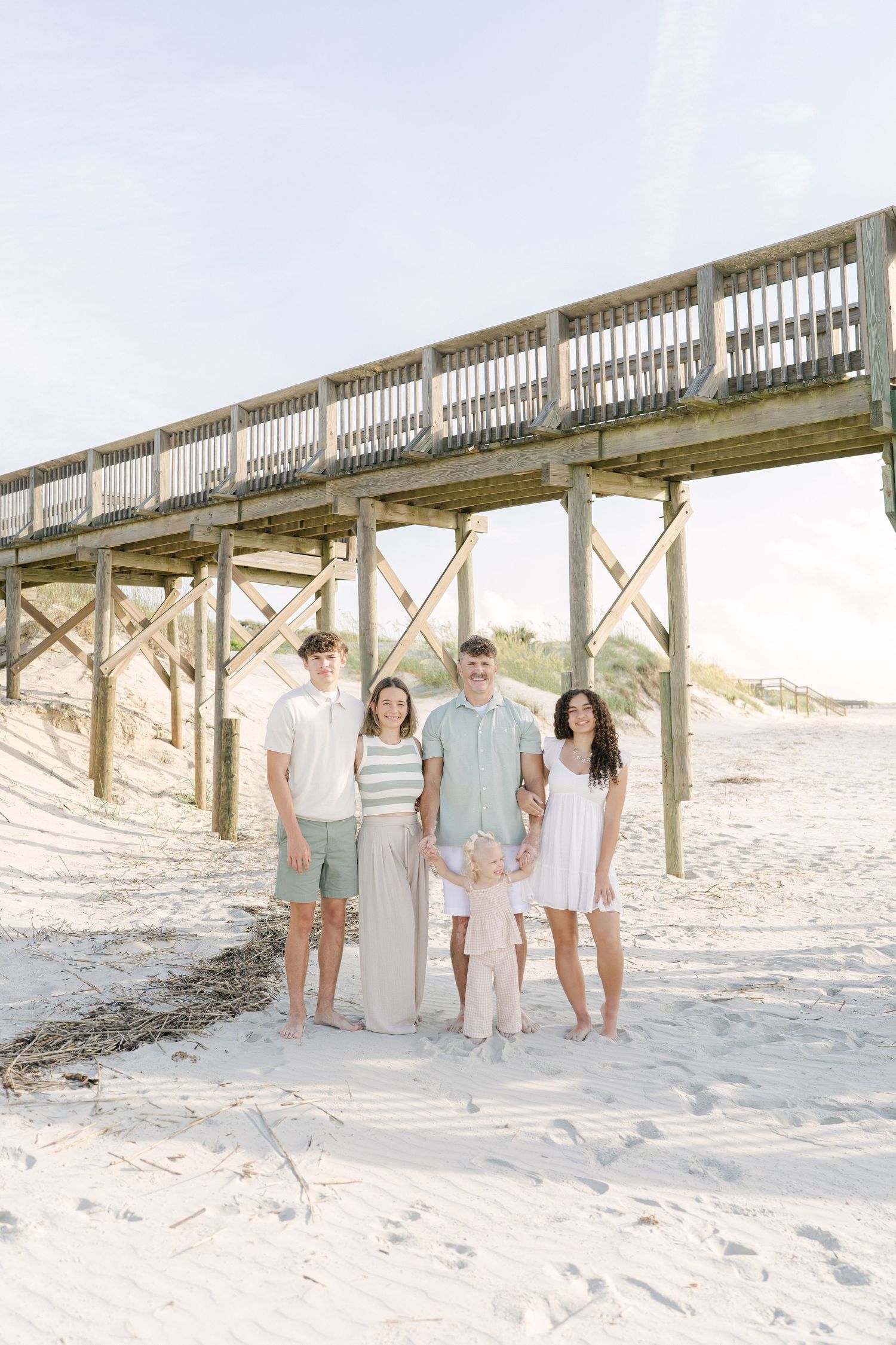 Family gathered beneath a beach pier during their Jekyll Island vacation photo session.
