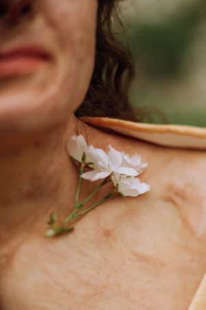 Close-up of a small cluster of delicate white blossoms resting on a woman's bare collarbone, with soft green blurred background.