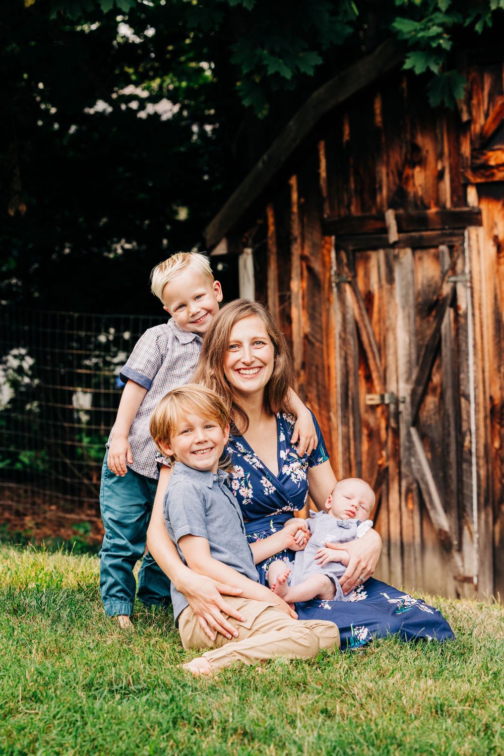 Casual family portrait on grass with rustic barn background during golden hour.