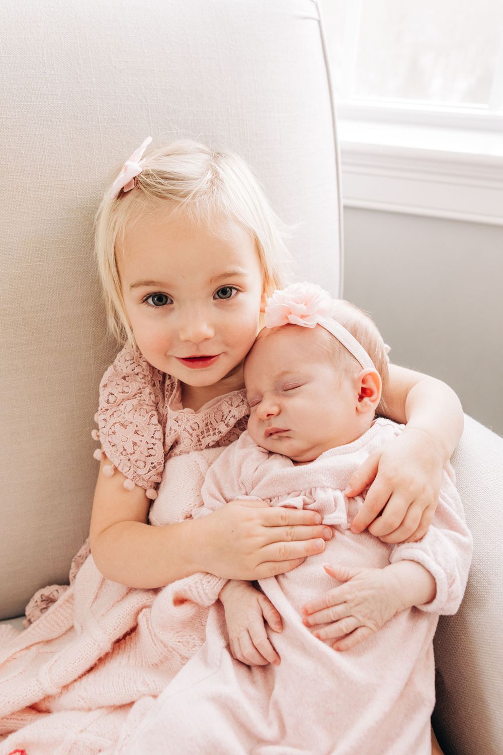 Sweet sibling embrace in soft pink and white tones.