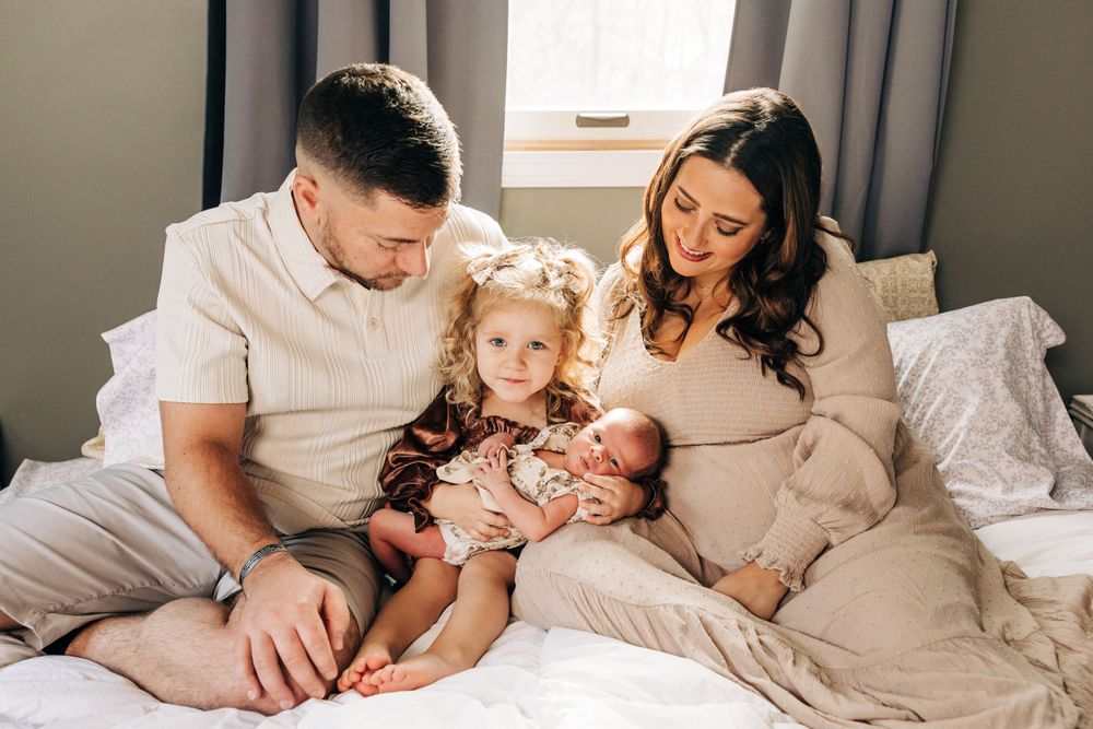 Intimate family moment captured on bed with natural window light in bedroom.
