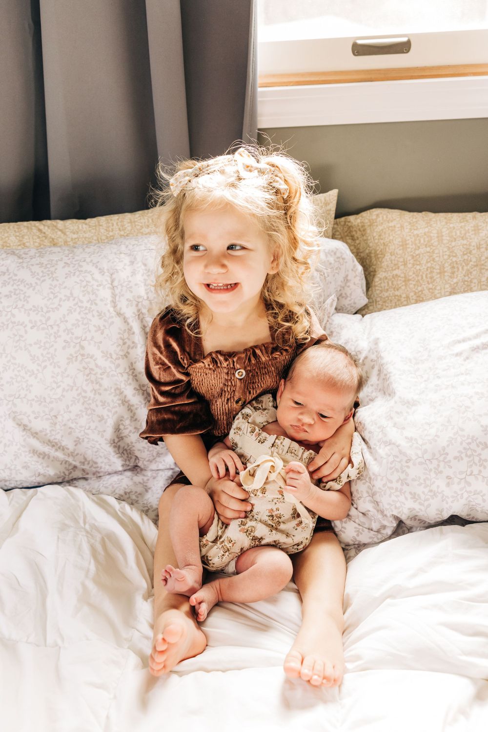 Siblings sharing tender moment on white bedding in bright natural light.