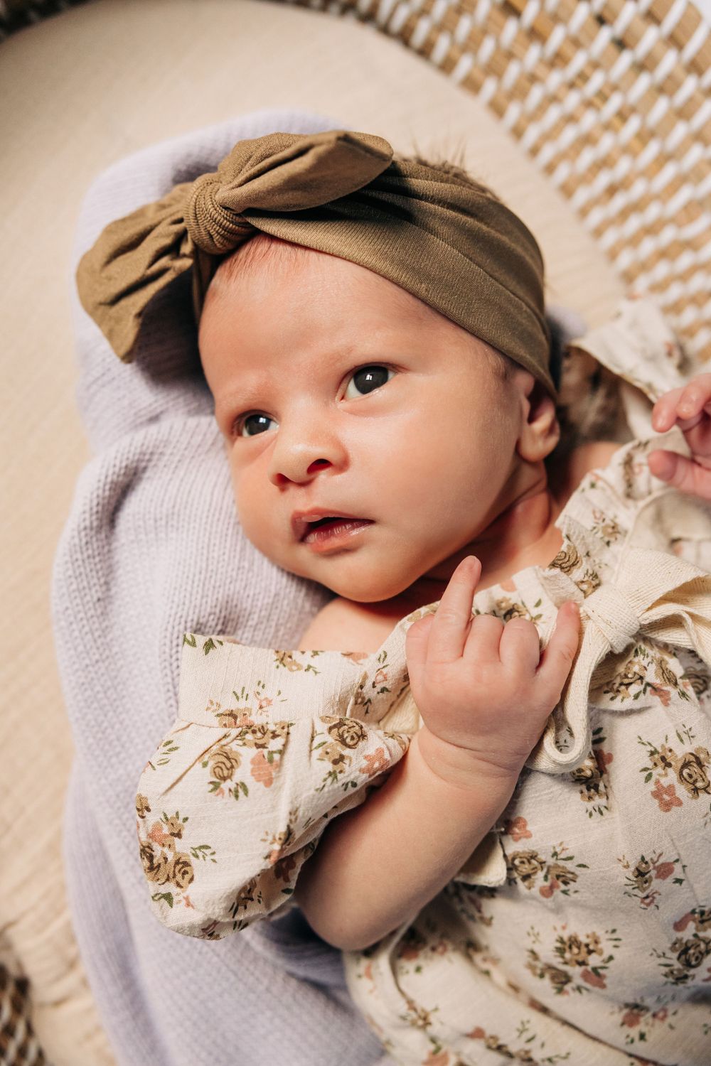 Baby wearing a tan bow headband and floral outfit lying on a soft blanket.
