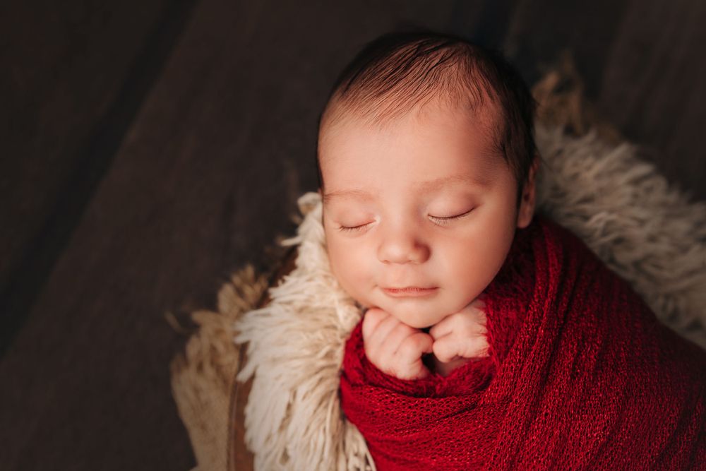 Close-up of sleeping newborn wrapped in red swaddle on textured blanket.